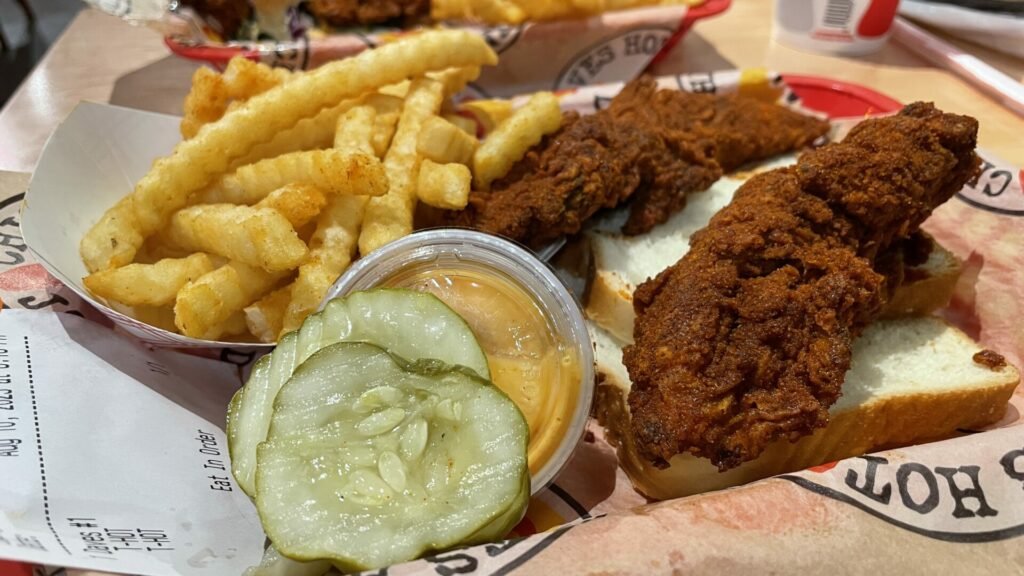 Closeup of Dave's Hot Chicken tenders, pickles, Dave's sauce, and fries